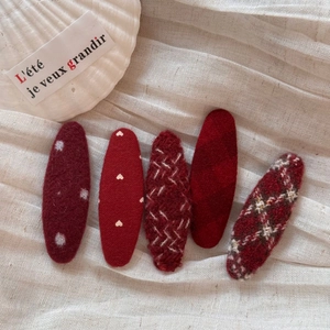 Close-up of five red fabric hair clips with polka dots, hearts, and wool felt textures
