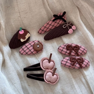 Flat lay of seven cute hair clips with bows and cherry patterns on beige fabric
