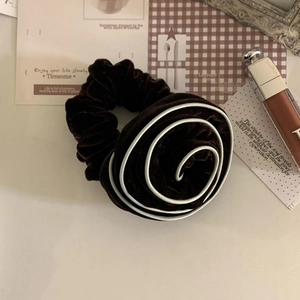 Detail view of a velvet rose hair scrunchie in deep brown with white stitched edges