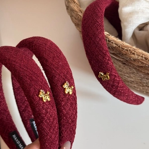 Detailed close-up of dark red braided headband with golden puppy metal charm and handmade label