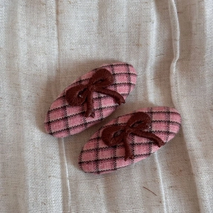 Close-up of pink plaid fabric hair clips with brown embroidered bows on linen background