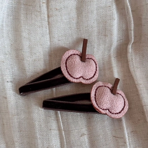Detail view of two pink apple hair clips with brown velvet lining on white linen cloth