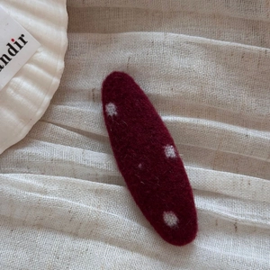 Close-up of deep red wool felt hair clip with white polka dots on soft fabric