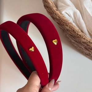 Detail view of red velvet headbands with golden heart charm on a woven background
