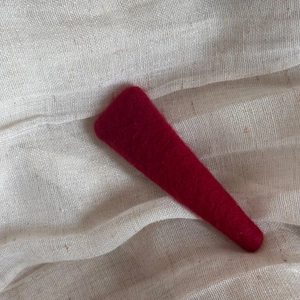 Close-up of deep red felt hair clip with soft texture on a beige fabric background