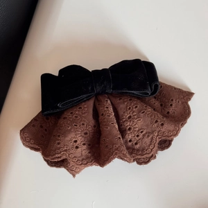 Dettaglio di fiocco in velluto nero vintage con pizzo ricamato marrone su sfondo bianco