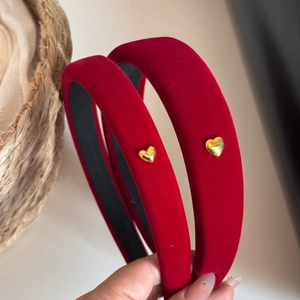 Macro detail of red velvet headband featuring a gold heart metal charm with logo engraving