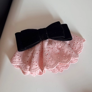 Dettaglio del fiocco in velluto nero con pizzo ricamato rosa e bordi a conchiglia