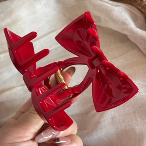 Detail of red bow hair claw clip with gold spring and smooth teeth on beige fabric