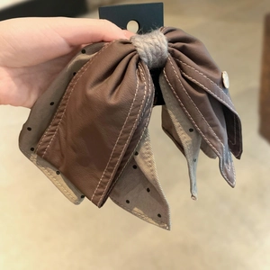 Close-up of brown polka dot bow hair clip showing leather texture and stitching detail