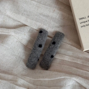 Close-up of gray plush wool hair clips with black polka dots on white linen fabric