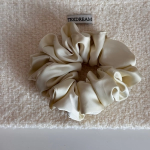 Gros plan sur un chouchou en satin crème avec texture soyeuse et étiquette de marque