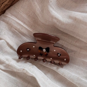 Detailed view of a brown bow hair claw clip with rhinestones on beige linen fabric