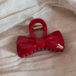 Detailed close-up of a glossy red bow hair claw clip with golden Barrette LaFrance text