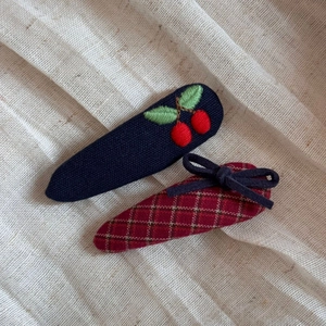 Detail of embroidered cherry and plaid bow fabric hair clips on linen background