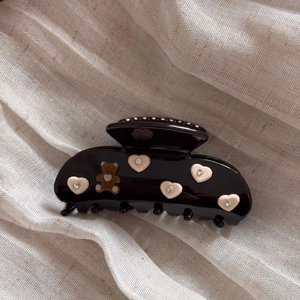 Detail of black acetate hair claw clip with heart patterns and bear ornament with rhinestones