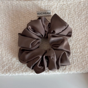 Vue détaillée d'un chouchou en satin marron foncé avec texture soyeuse sur fond en tissu