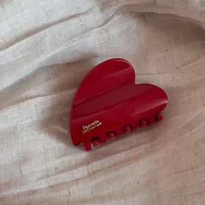 Detail of red heart-shaped hair claw clip with golden lettering on fabric background