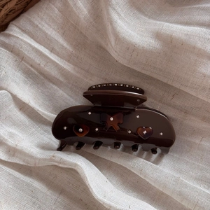 Detailed close-up of tortoise shell acetic hair claw with rhinestones and bow on beige cloth