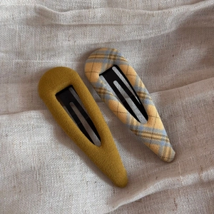 Close-up of mustard yellow and blue plaid fabric BB hair clips on a soft beige background