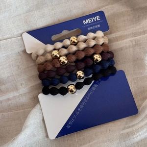 Detail of five elastic hair ties with gold beads on display card in earthy tones