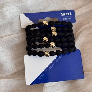 Detailed view of six black elastic hair ties with gold beads on a branded display card
