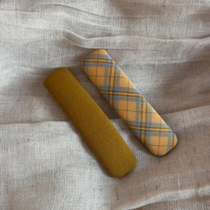 Detail of fabric plaid and solid mustard yellow rectangle hair clips on beige linen background