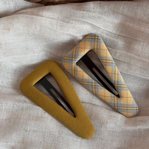 Detail view of mustard green and plaid fabric triangle hair clips on linen background