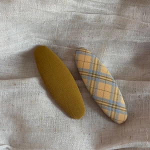 Close-up of two fabric hair clips featuring mustard yellow and blue plaid patterns