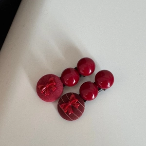 Dettaglio di due fermagli per capelli in velluto bordeaux con fiocchi e perline rosse