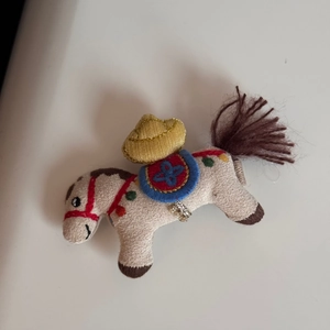 Dettaglio di un ciondolo a forma di pony in tessuto beige con cappello di paglia
