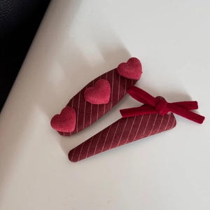 Dettaglio di fermagli rossi con fiocchi, cuori e trama di tessuto a righe per capelli