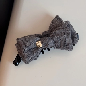 Detailed macro view of dark grey layered lace bow hair claw with gold metal emblem charm