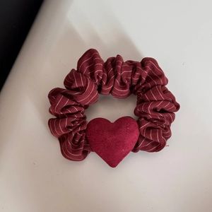 Dettaglio di un elastico per capelli bordeaux a righe con decorazione a cuore rosso