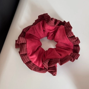 Dettaglio di scrunchie in velluto rosso scuro con bordi a balze plissettate e texture morbida