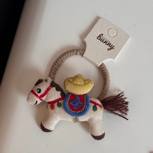Dettaglio dell'elastico per capelli con cavallo ricamato, mini cappello e nappa colorata