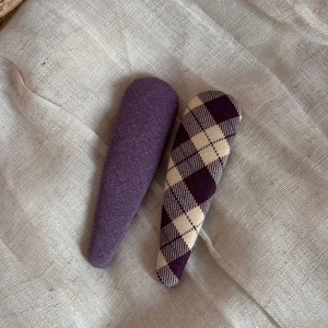 Detail of two handmade purple fabric hair clips with plain and plaid patterns on linen