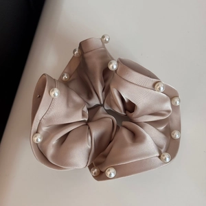 Detail of champagne satin scrunchie with white pearl accents and elegant silk texture