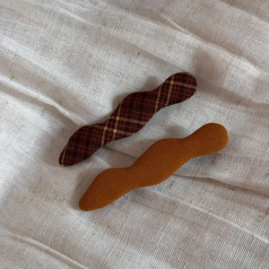 Close-up of wavy plaid and solid ginger fabric hair clips on a soft beige background