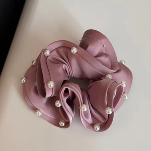 Close-up of pink satin scrunchie with white pearl accents and elegant ruffled edges