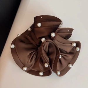 Detailed close-up of brown satin scrunchie featuring elegant white faux pearl edge accents