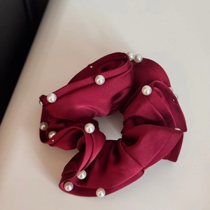 Detail of burgundy satin scrunchie with white pearl accents on light cream background