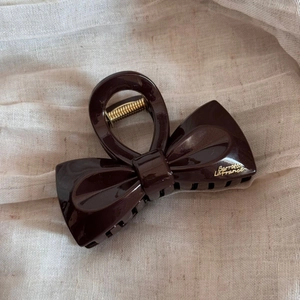 Détail d'une pince à cheveux nœud marron avec lettrage doré sur tissu beige