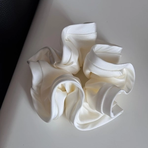 Detailed view of large white satin scrunchie with elegant ruffled flower-like design