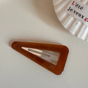 Nahaufnahme einer dreieckigen bernsteinfarbenen Acetat-Haarspange mit Goldbeschriftung