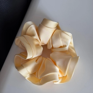 Detailed view of the layered ruffles on a glossy cream satin oversized hair scrunchie