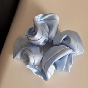 Detailed view of the smooth light blue satin fabric and ruffled texture of the hair scrunchie