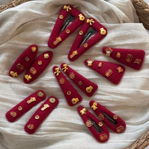 Red felt hair clips with golden Chinese lucky symbols and charms on white fabric