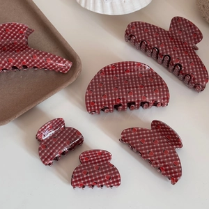 Detail view of red plaid hair claw clips with strawberry patterns on a white surface