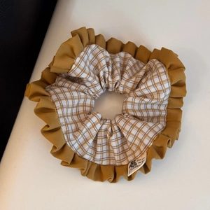 Close-up of yellow pleated scrunchie with plaid patterns and handmade label detail